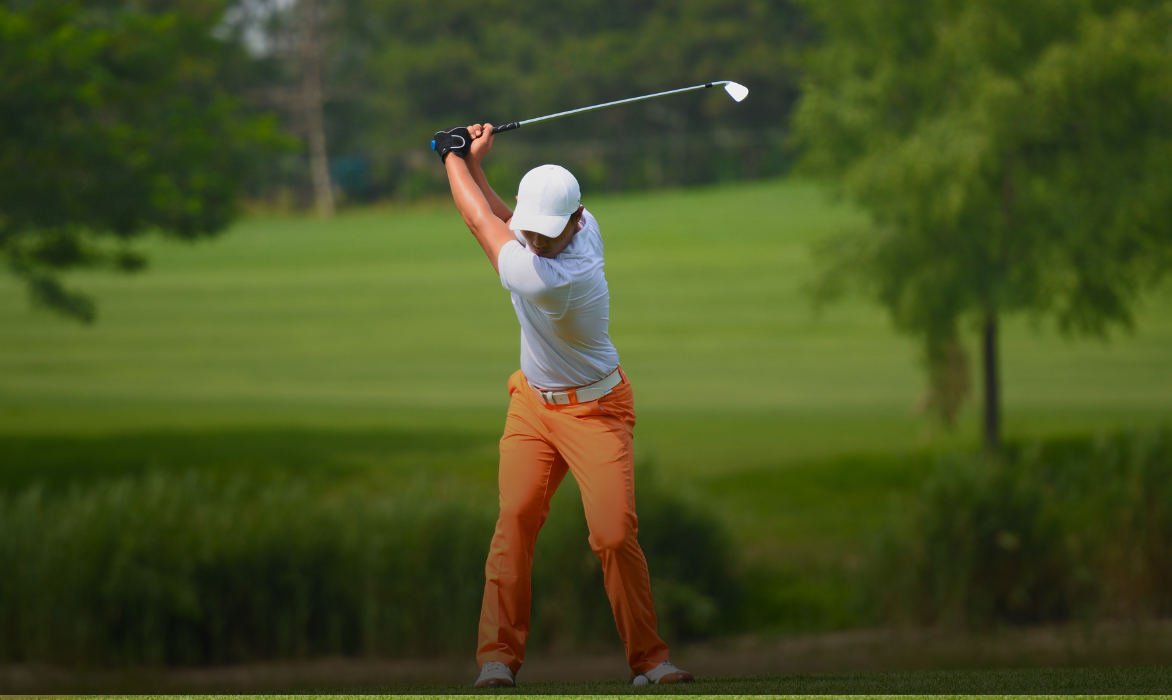 Golfer in mid-swing on a tree-lined fairway