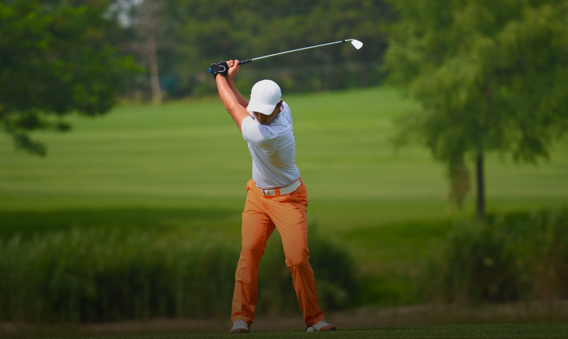 Golfer mid-swing on a tree-lined fairway