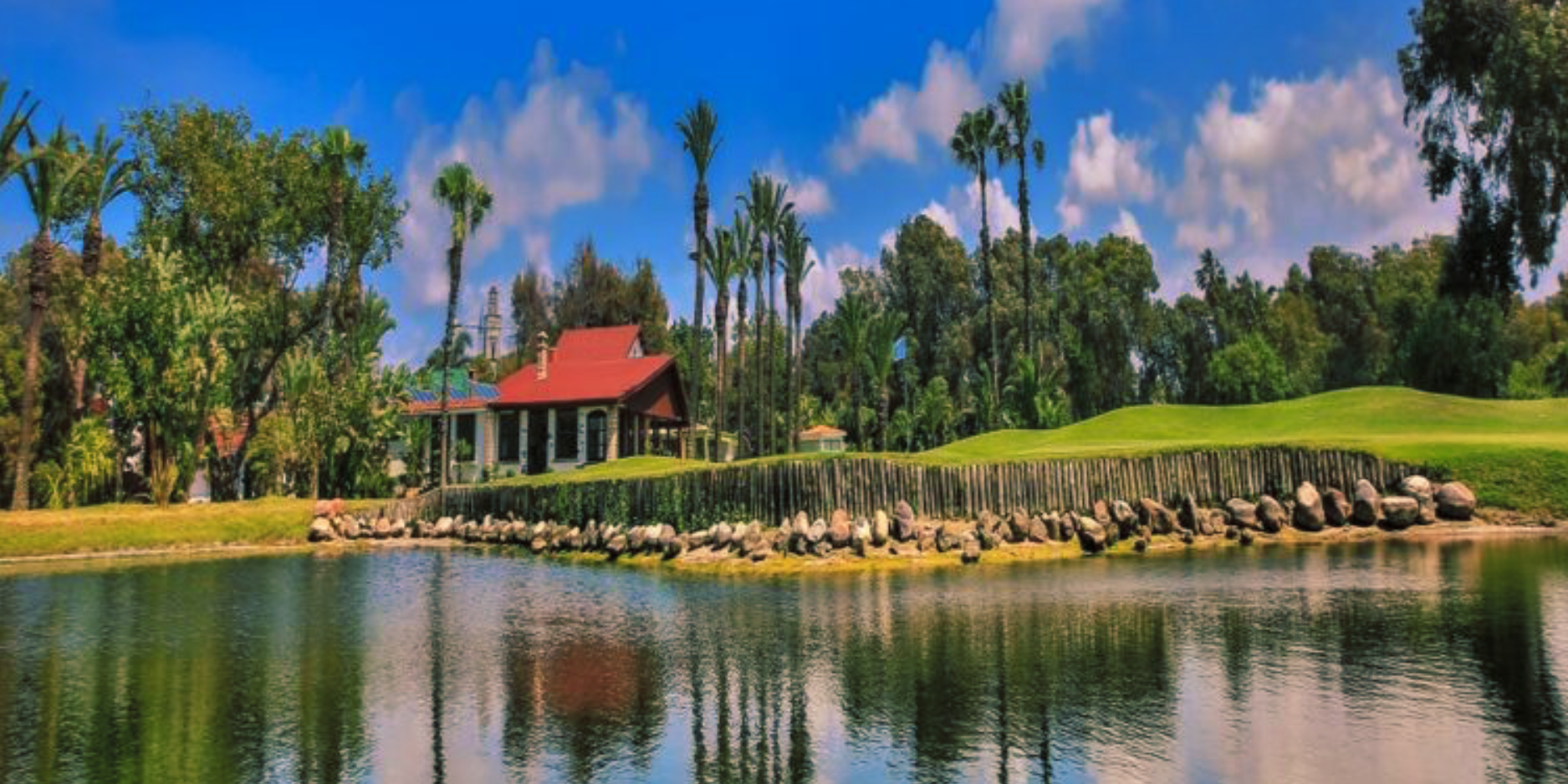Red-roofed clubhouse beside a palm-lined lake