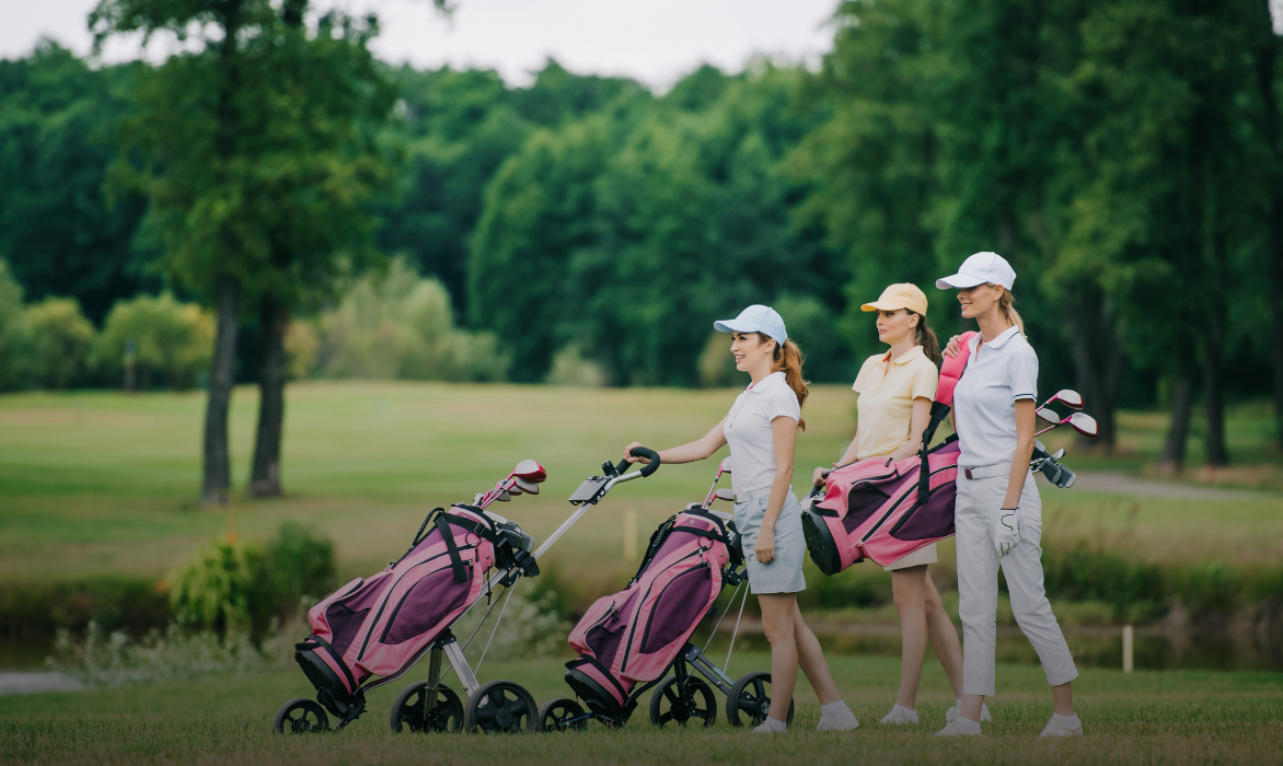 Three women golfers with their trolleys on a tree-lined course