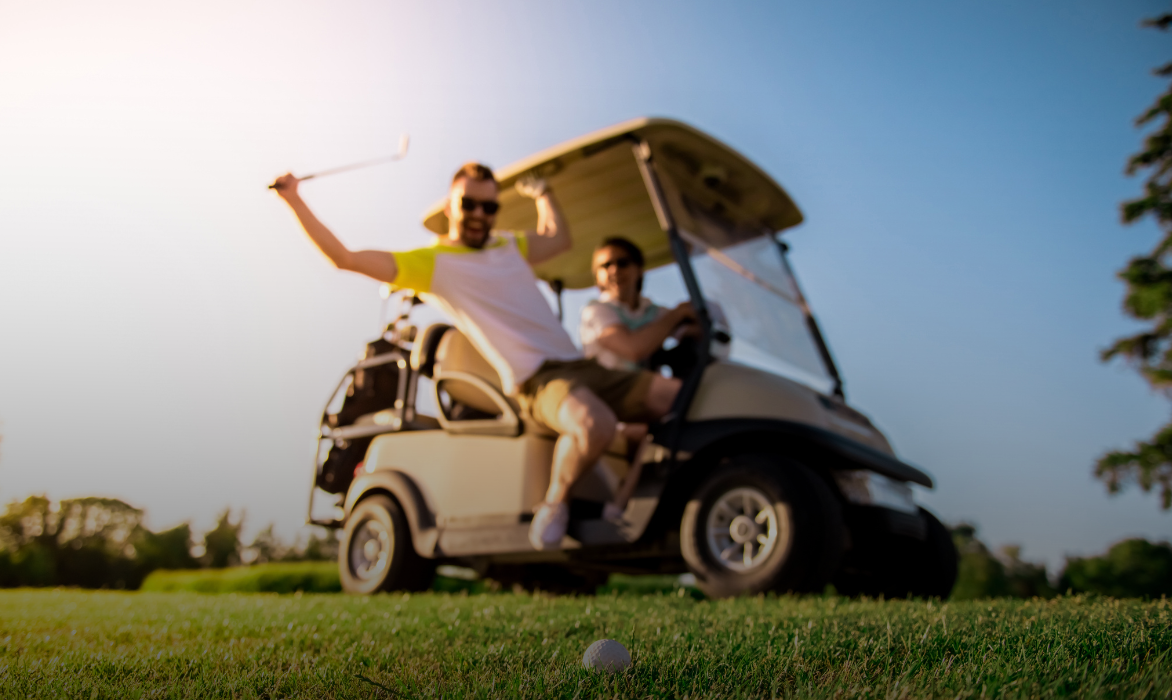 Two golfers in a golf buggy on a course, one raising his club