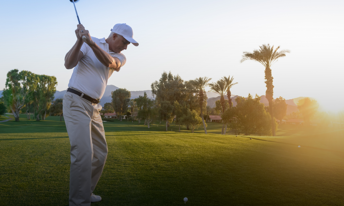 Golfer driving off the tee at sunset, palm trees behind