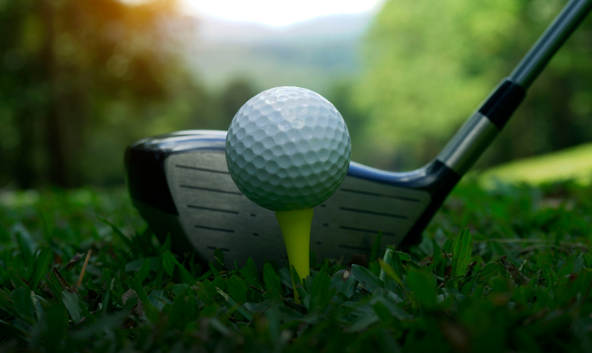 Golf ball on a tee with a club head behind it