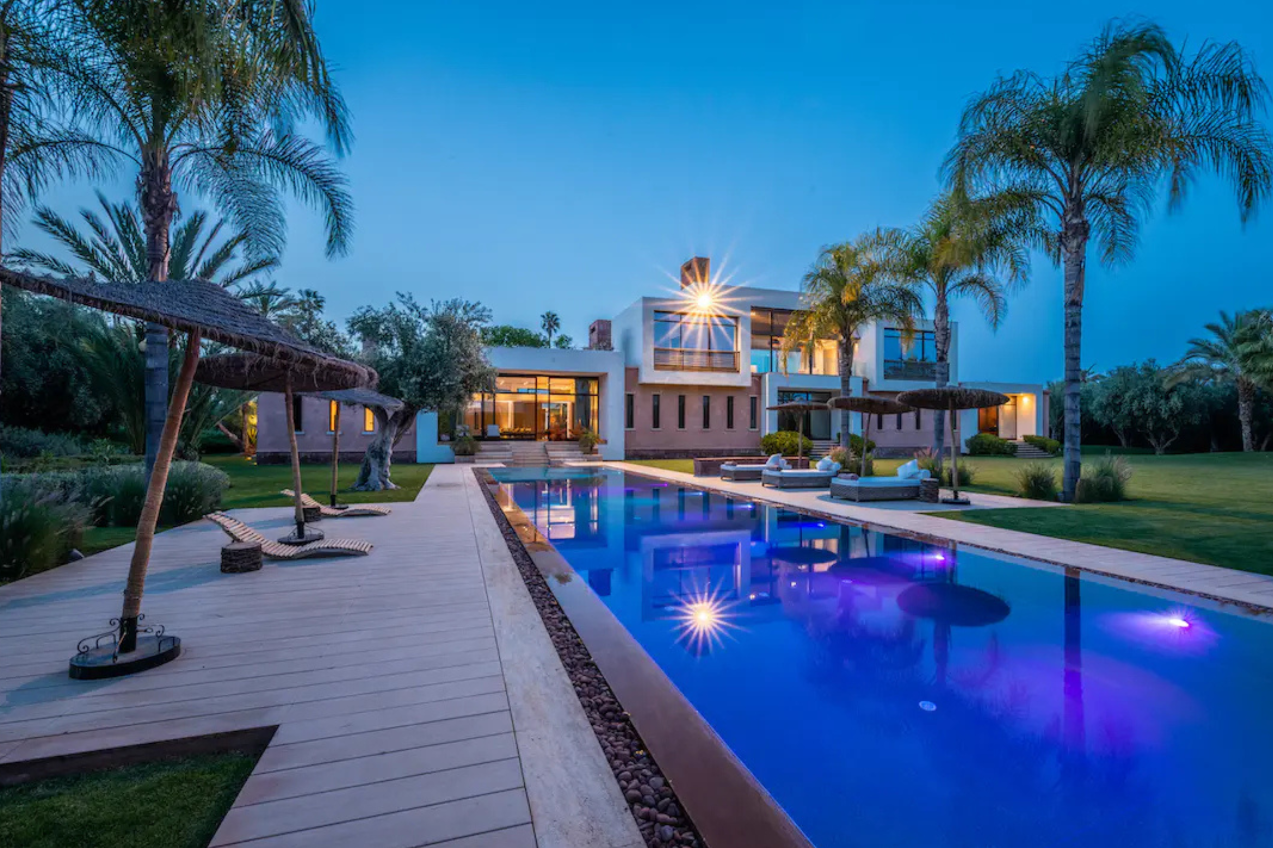 Villa with a palm-lined swimming pool, lit up at dusk