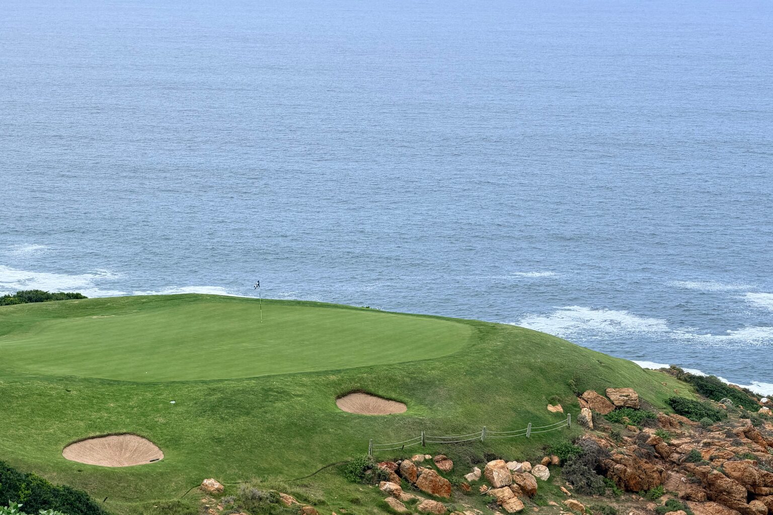 Parcours de golf en bord d'océan, bunkers de sable clair et green face à la mer