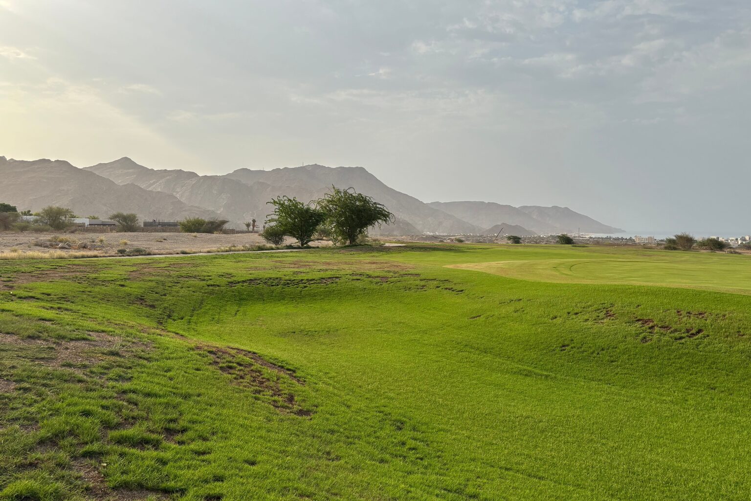 Green d'un parcours de golf bordé de collines arides, sous un ciel voilé