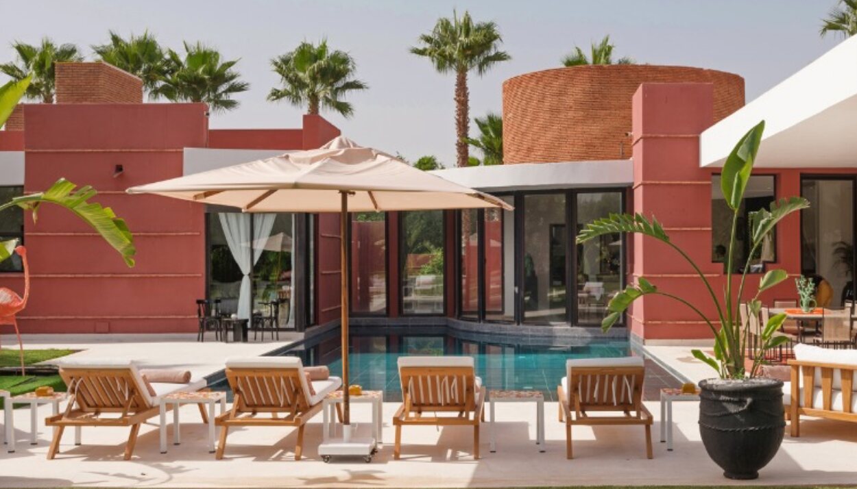 Red-walled villa with a pool, wooden sun loungers, a parasol and palm trees